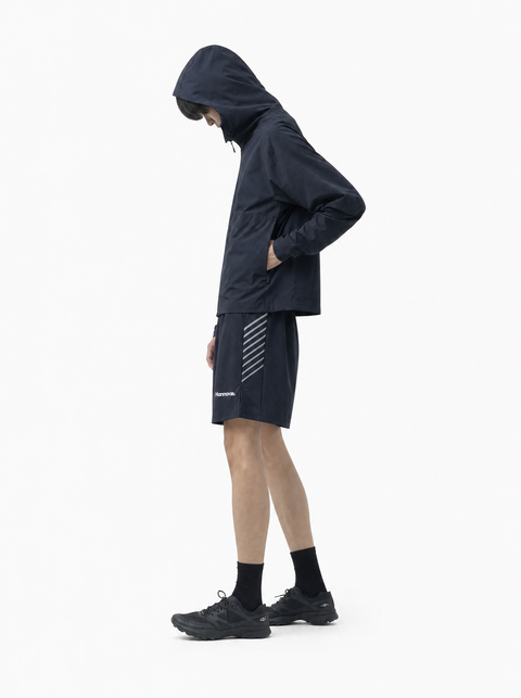 A model wearing a dark navy hooded athletic jacket, matching navy shorts with white diagonal stripes, black socks, and trail running shoes, shown in profile against a plain white background.