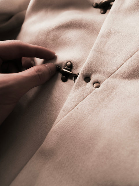 Close-up of a hand buttoning a beige Dune Hanfu jacket coat by hannovae with a focus on texture and detail.