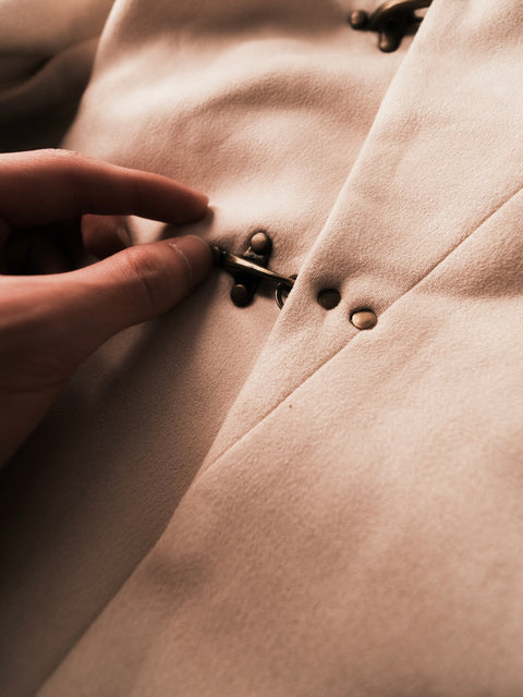Close-up of a hand buttoning a beige coat with a focus on texture and detail.