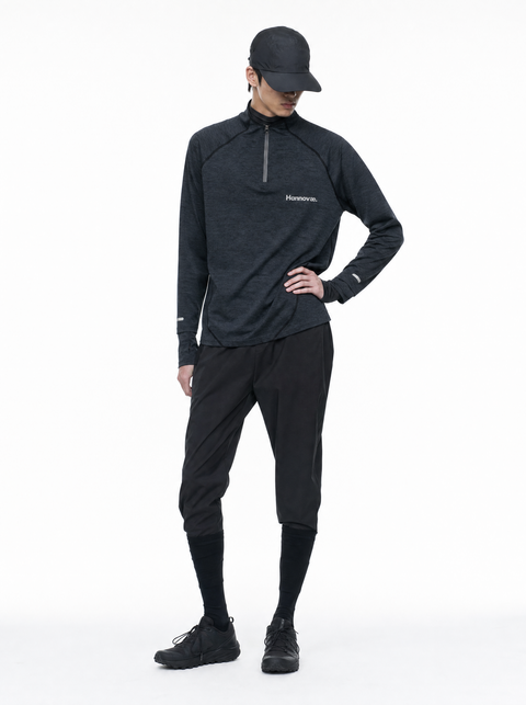 A man modeling a dark gray long-sleeve quarter-zip athletic pullover, black running pants, black socks, and a black cap against a plain white studio background.
